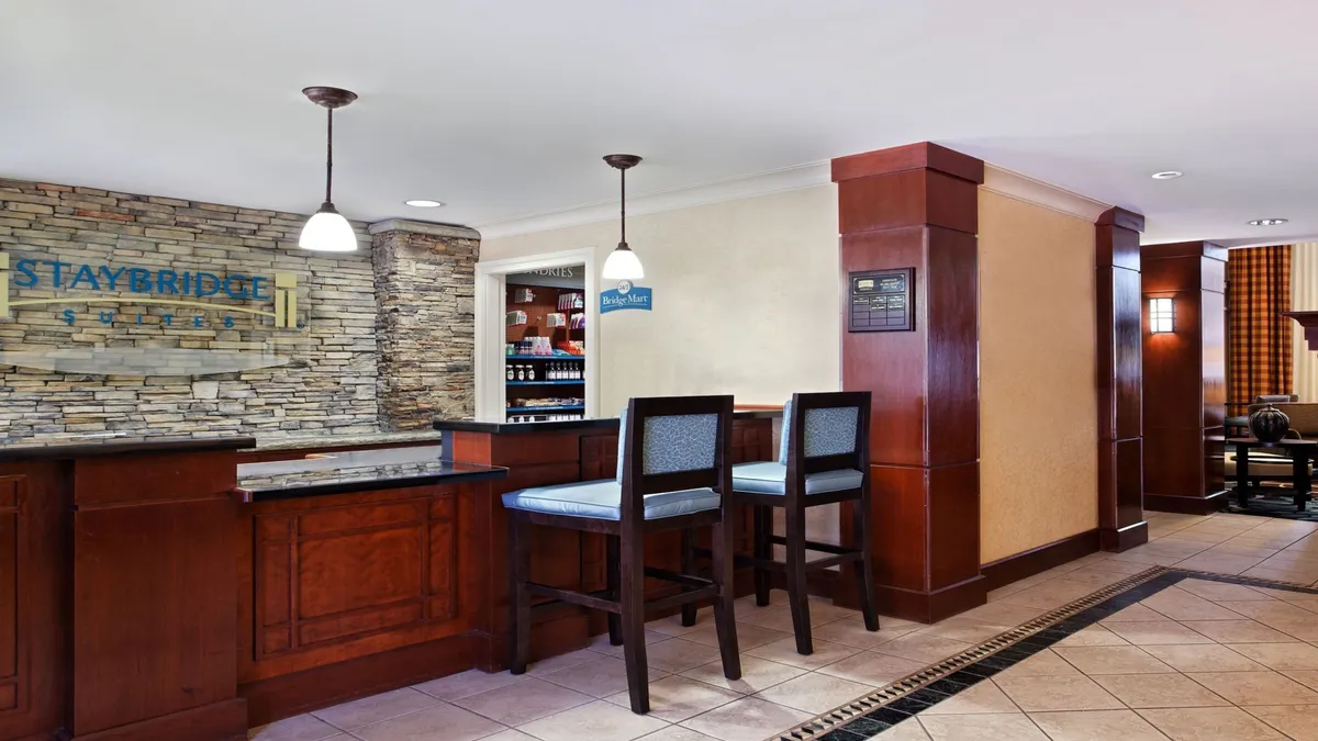 The image features a stylish reception desk with a stone accent wall, bar stools, and striking light fixtures. The space is welcoming and friendly, ideal for check-ins, socializing, or enjoying a refreshment after a long day.