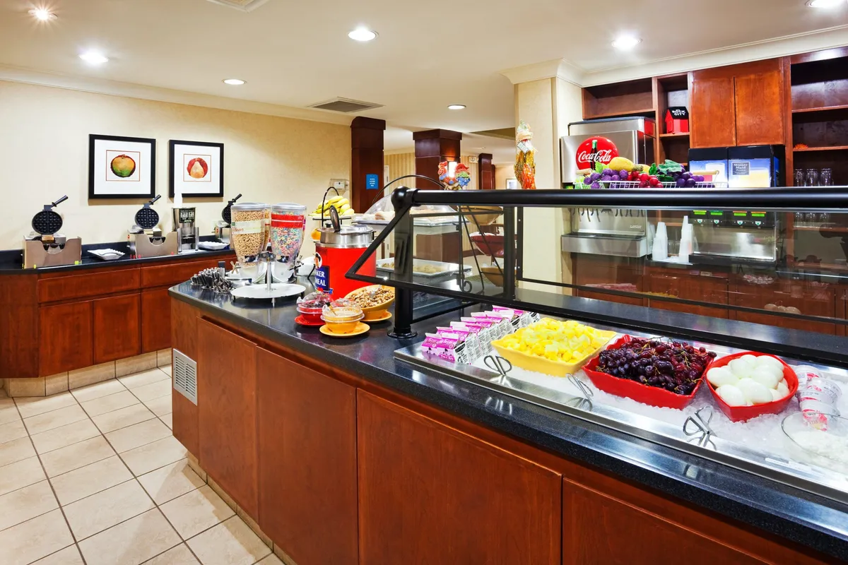 This image displays a buffet counter lined with a variety of breakfast items and a beverage station, set against decorative artwork. The atmosphere is cheerful and relaxed, with guests enjoying self-service dining and social interaction.