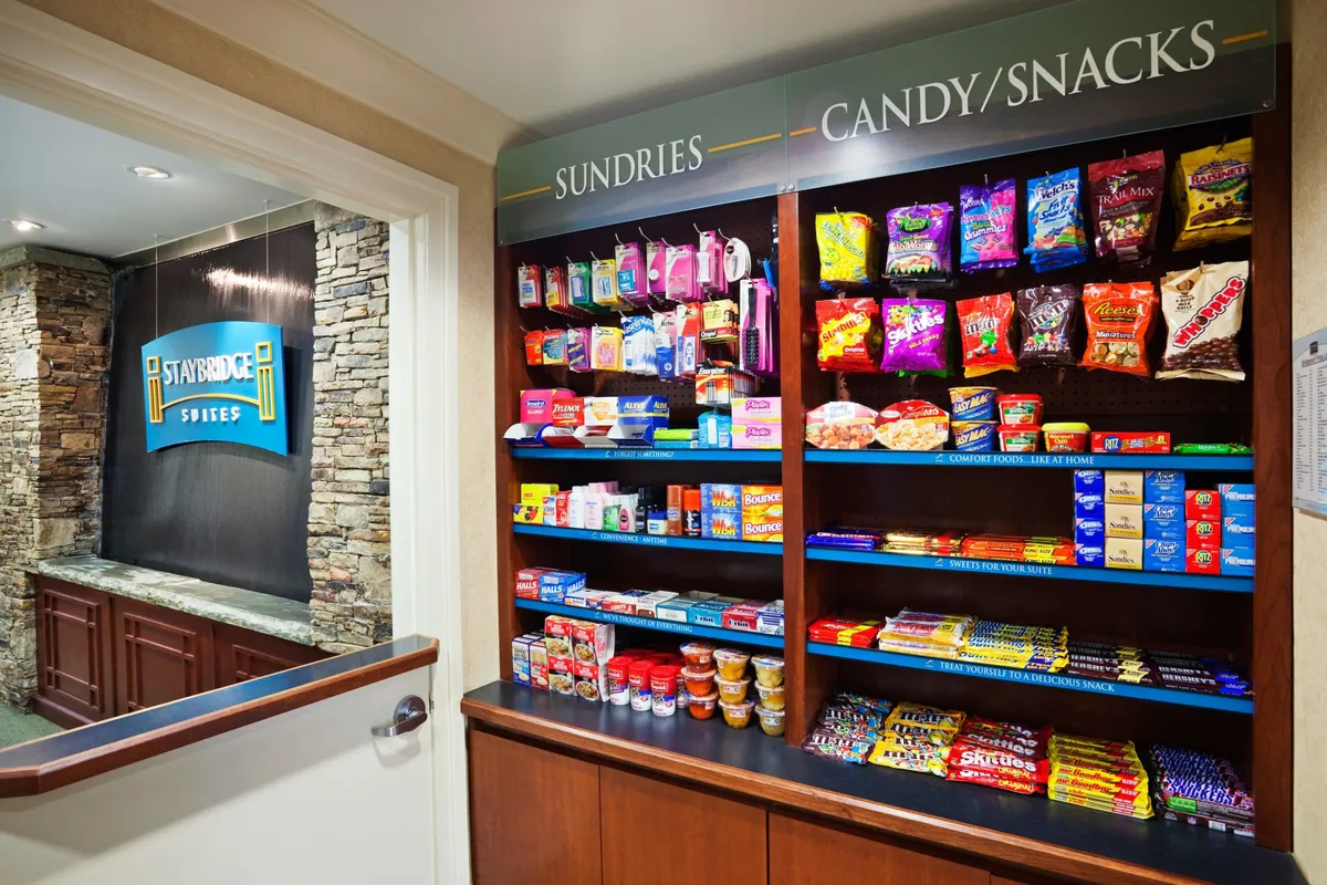 A bright, friendly interior view of the reception area featuring well-stocked snack shelves against a stone wall, providing guests with easy access to treats and essentials before or after city excursions. The atmosphere is casual and approachable, suggesting convenience for families on the go.