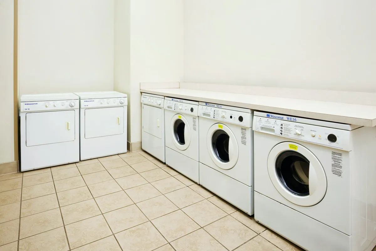 A practical and clean laundry facility featuring washing machines, dryers, and a countertop for sorting and folding clothes. The space is well-lit and organized, emphasizing the ease of keeping clothes fresh during extended stays.
