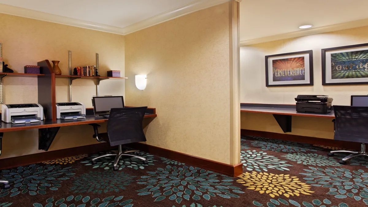 A dedicated workspace with computers, printers, bookshelves, and colorful carpeting, designed for productivity and focus. The area is well-lit and organized, encouraging both work and study.