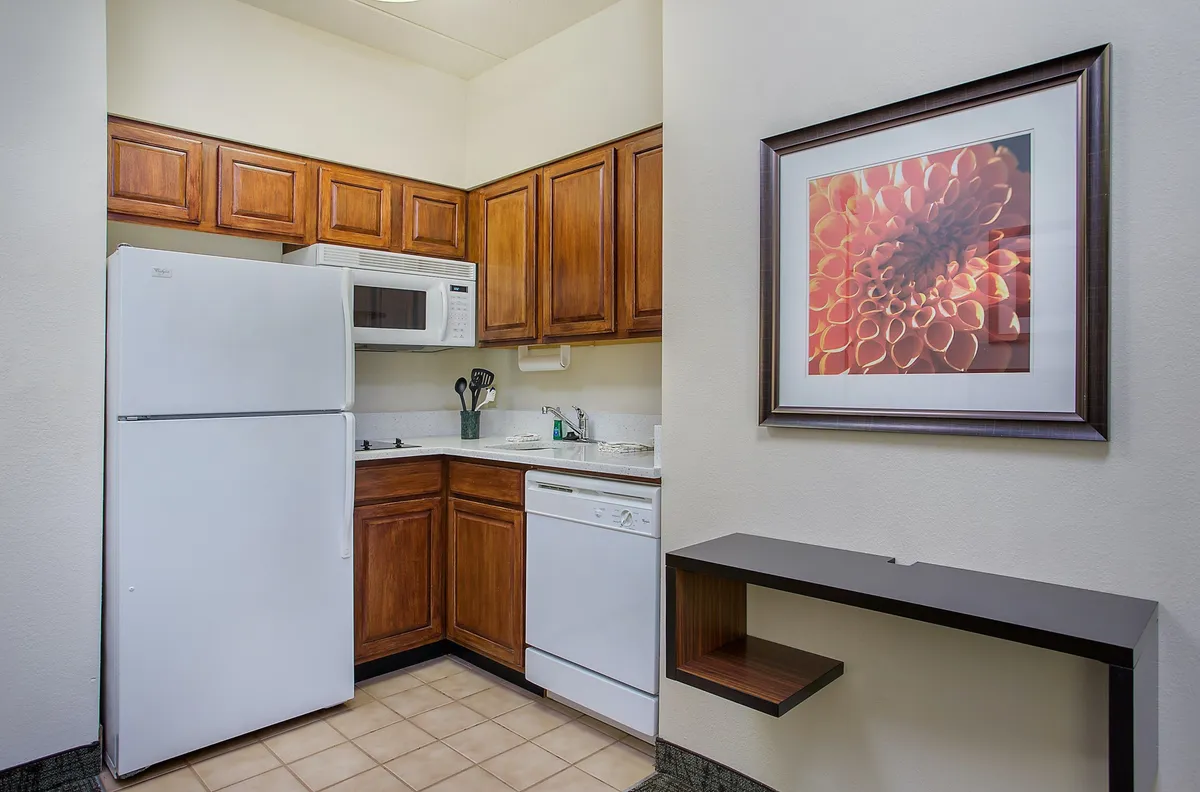 A bright, inviting kitchen space featuring wooden cabinetry, a full suite of appliances (stove, microwave, dishwasher, and coffee maker), and decorative artwork on the wall. The kitchen exudes a welcoming mood, with ample workspace and room for meal preparation or casual dining.