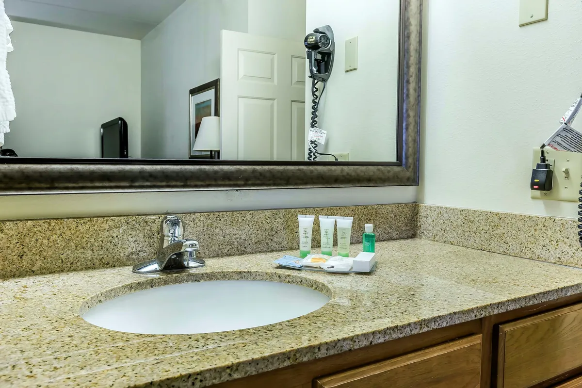 An inviting, well-appointed bathroom showcasing a granite countertop, large mirror, sink, and neatly arranged complimentary toiletries. The ample space makes the area functional for morning routines, and the setup includes fresh towels and a hairdryer within easy reach.